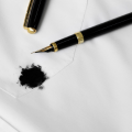 Uma caneta-tinteiro preta e dourada ao lado de uma mancha de tinta preta em um tecido branco.