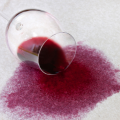 Taça de vinho tombada derramando vinho tinto sobre um tecido claro, formando uma grande mancha de vinho.