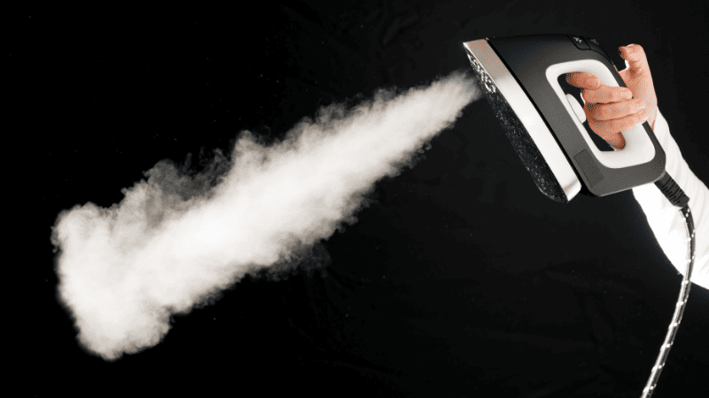 Ferro de passar liberando jato intenso de vapor em direção oposta à pessoa.