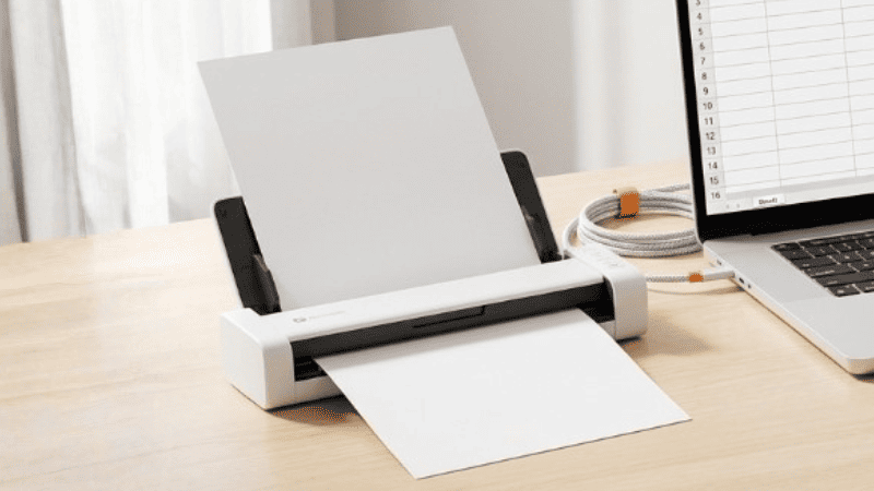 Scanner portátil digitalizando uma folha sobre a mesa de um home office.